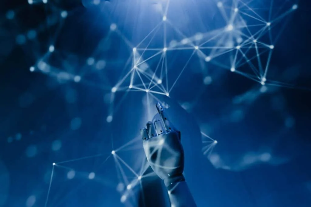 robot-pointing-on-a-wall A robotic hand reaching into a digital network on a blue background, symbolizing AI technology.